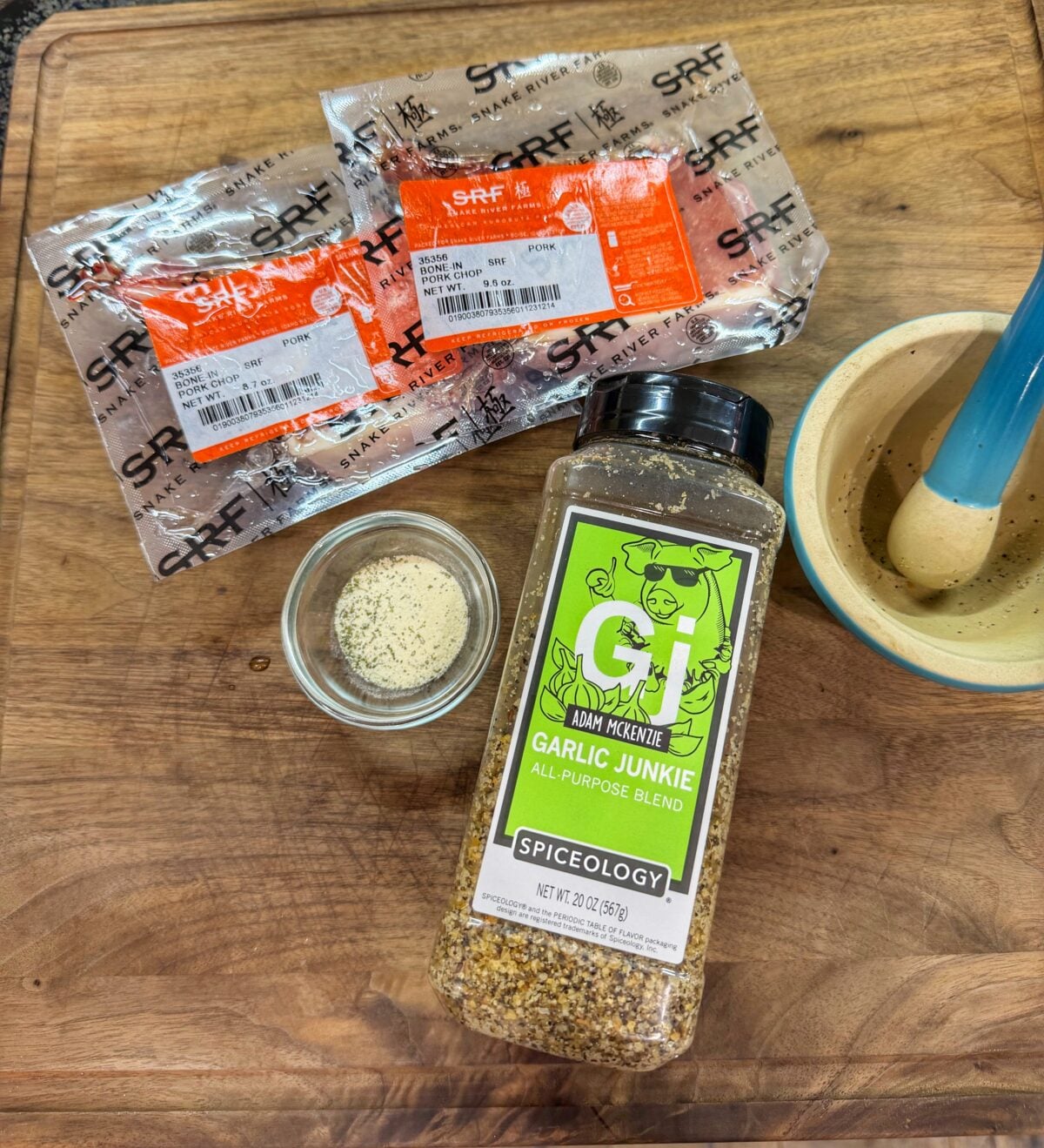 Ingredients for garlic ranch pork chops including Kurobuta pork chops, garlic seasoning, ranch powder, and mortar and pestle.