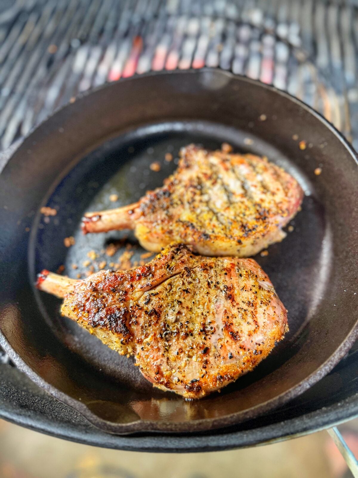 Pork chops searing in a hot cast iron skillet after being cooked on the cool part of the grill.