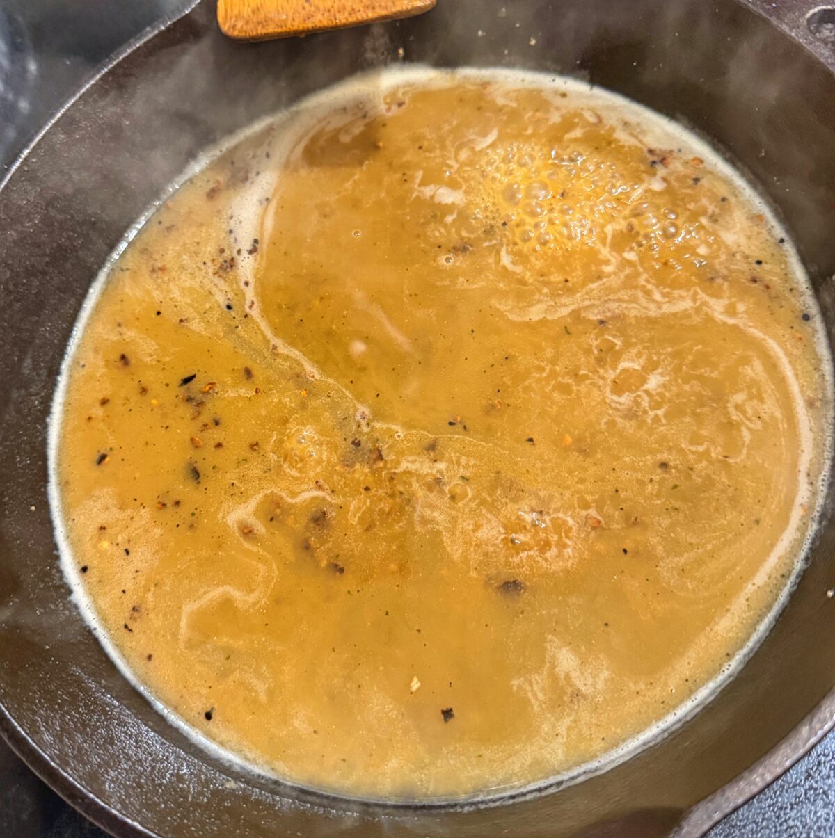 Creamy garlic ranch sauce simmering in a cast iron skillet made from pork drippings and broth.