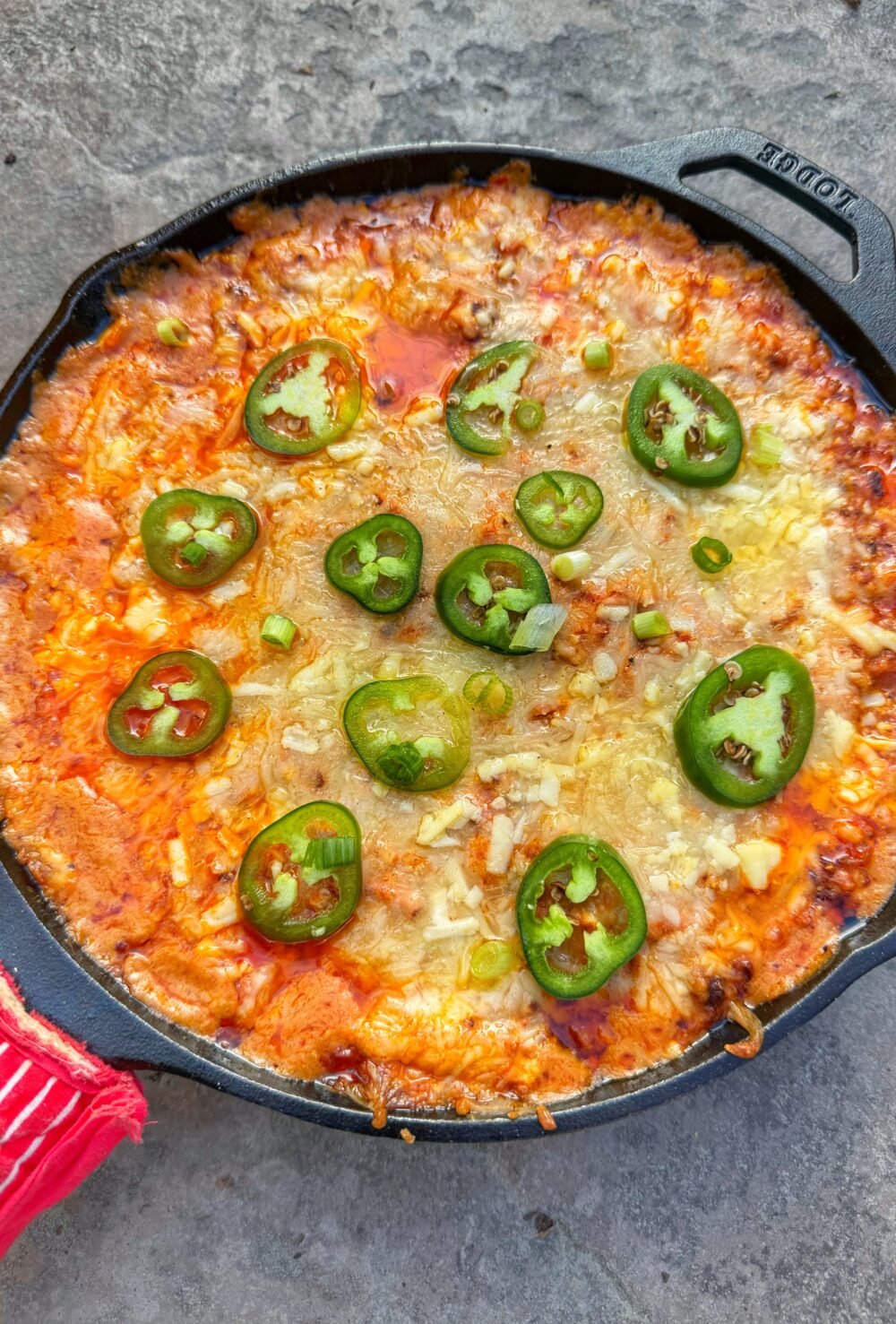Cast iron skillet filled with chili cheese hot dog dip topped with sliced jalapeños, melted cheese, and visible chili oil on the surface.