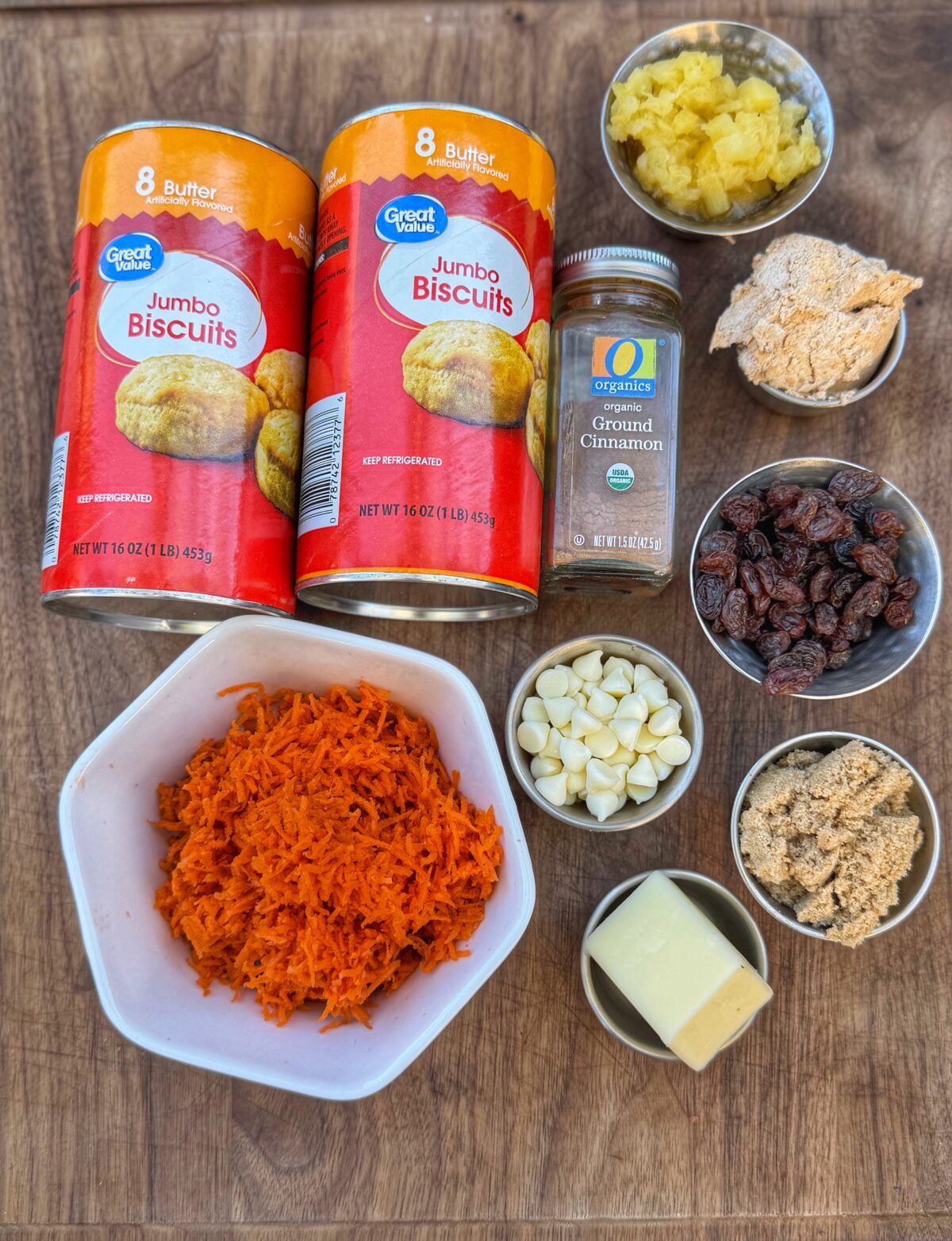 Ingredients for carrot cake monkey bread including biscuit dough, shredded carrots, pineapple, raisins, brown sugar, cinnamon, butter, and white chocolate chips.