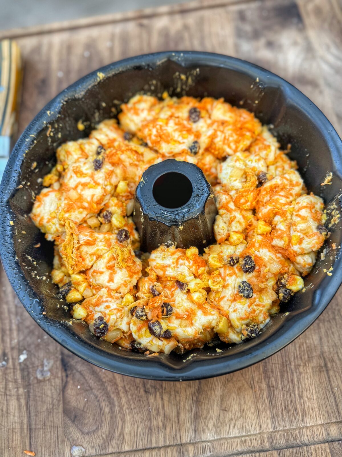Bundt pan filled with biscuit dough pieces mixed with shredded carrots, raisins, pineapple, and white chocolate chips before baking.