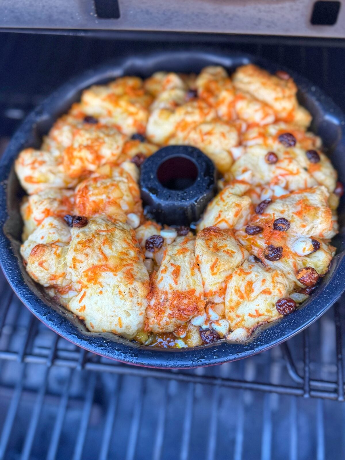 Bundt pan filled with carrot cake monkey bread baking inside a pellet grill.