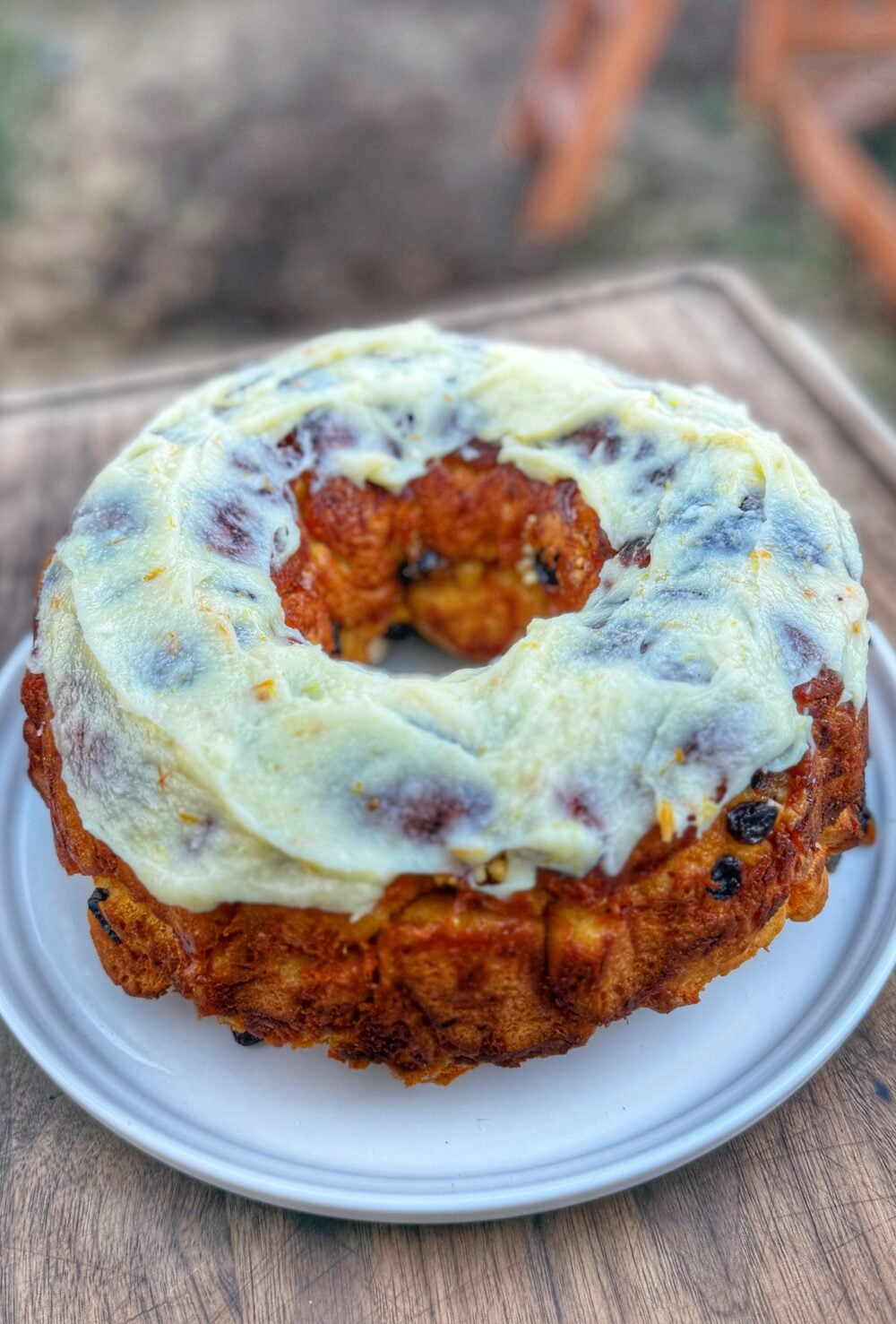 Carrot cake monkey bread topped with cream cheese icing served on a white plate outdoors.