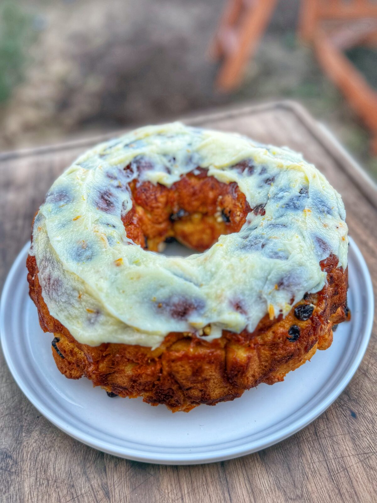 Carrot cake monkey bread topped with cream cheese icing served on a white plate outdoors.