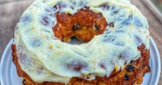 Carrot cake monkey bread topped with cream cheese icing served on a white plate outdoors.
