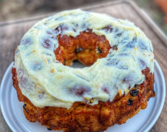 Carrot cake monkey bread topped with cream cheese icing served on a white plate outdoors.