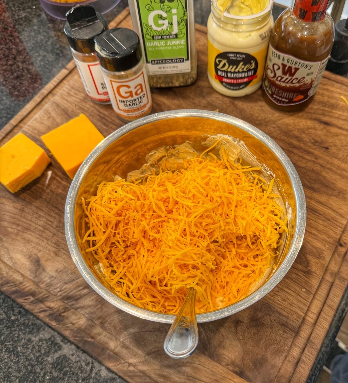 Large amount of freshly shredded cheddar cheese added on top of a creamy mixture in a metal mixing bowl.