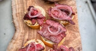 Toasted crostini topped with sliced steak, pimento cheese, and pickled red onions on a wooden serving board.