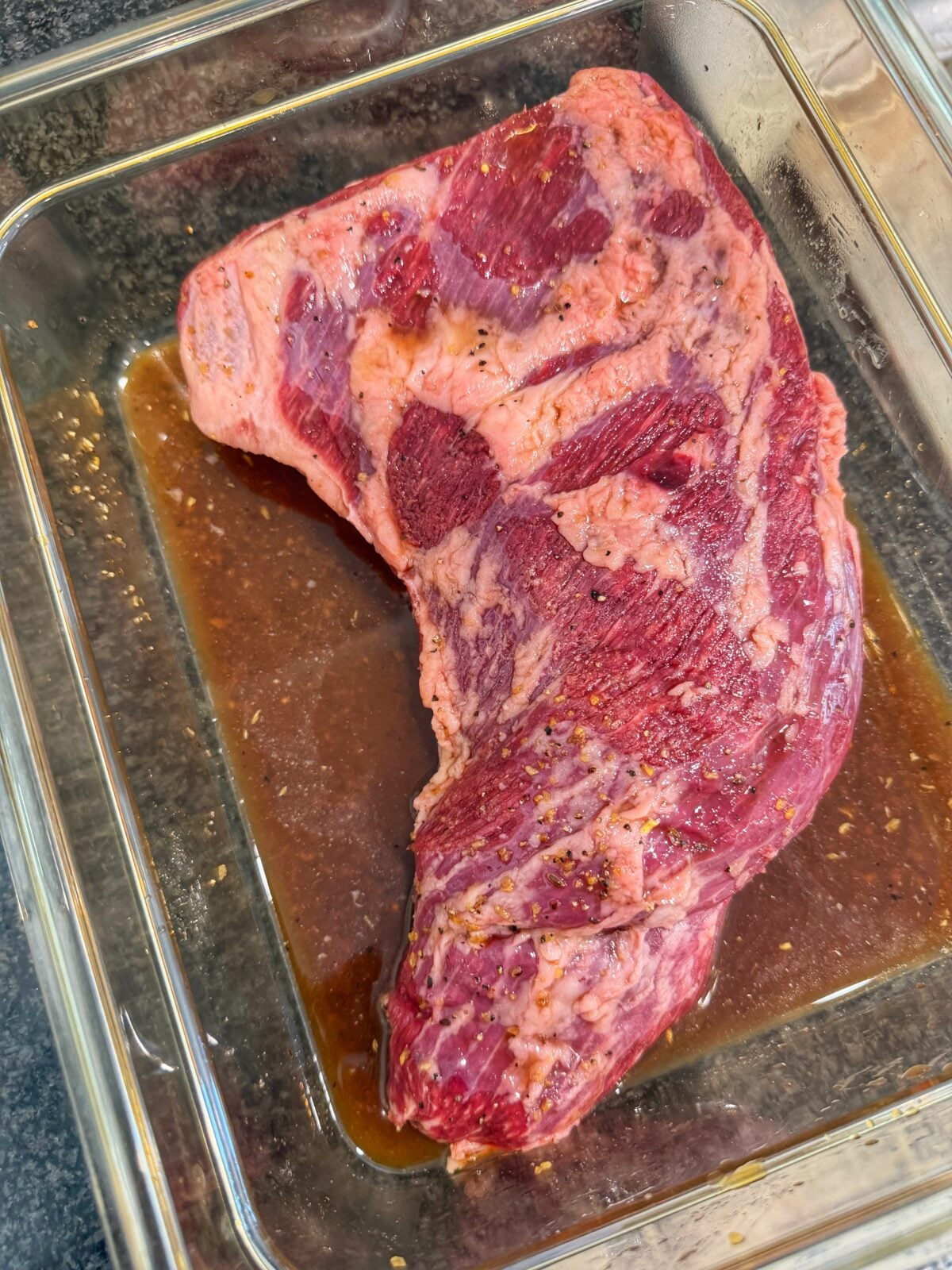 Tri tip roast sitting in a dish coated in marinade.