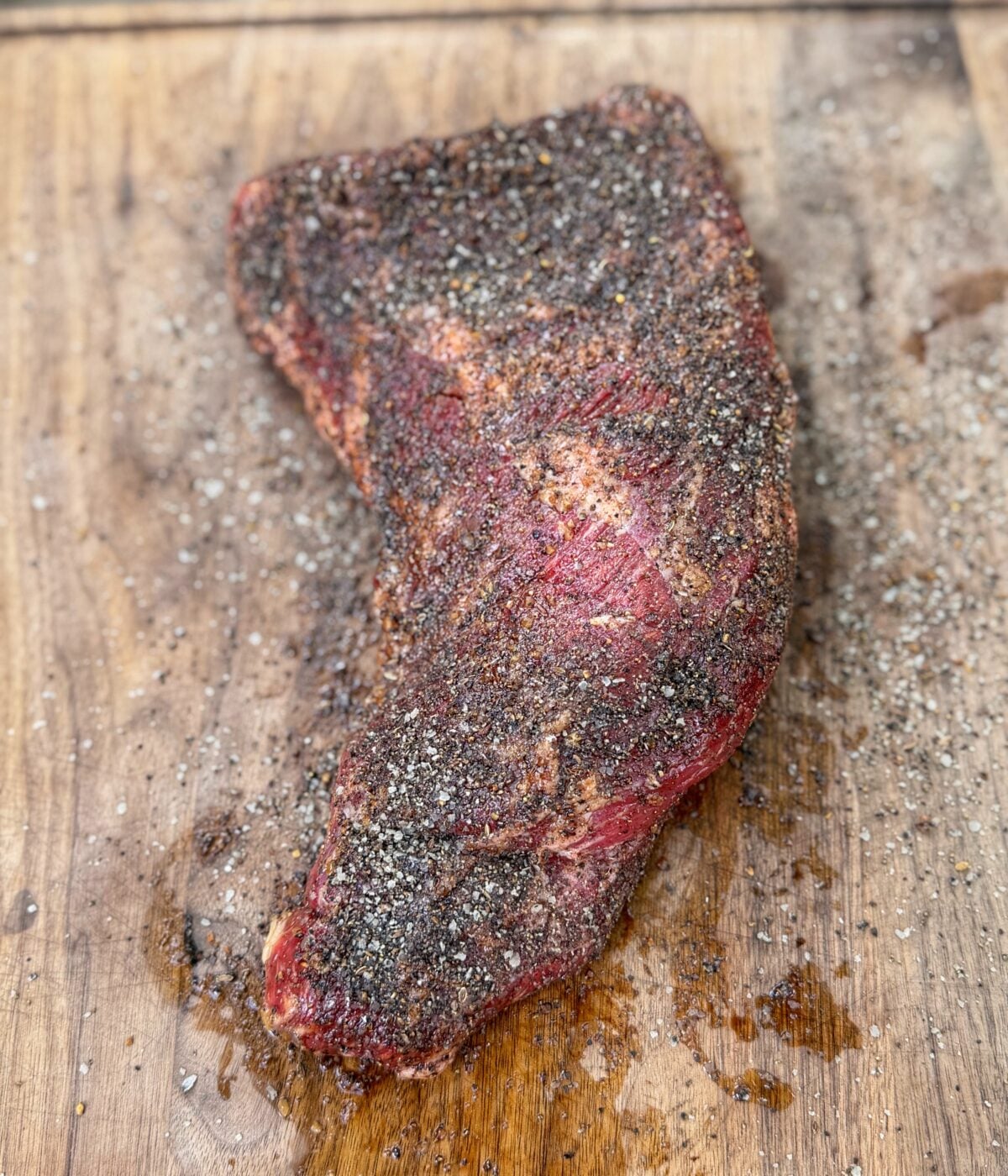 Seasoned tri tip roast resting on a cutting board before cooking.