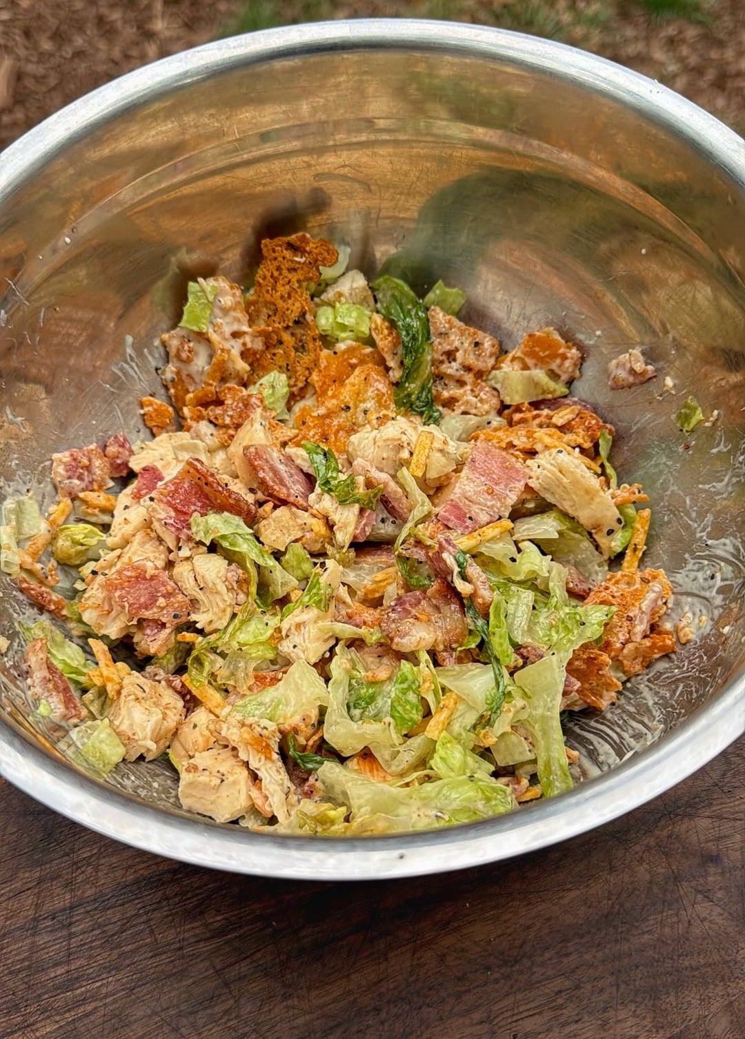 Grilled chicken Caesar filling with bacon, romaine, crispy parmesan, jalapeño potato straws, and Caesar dressing mixed in a metal bowl.