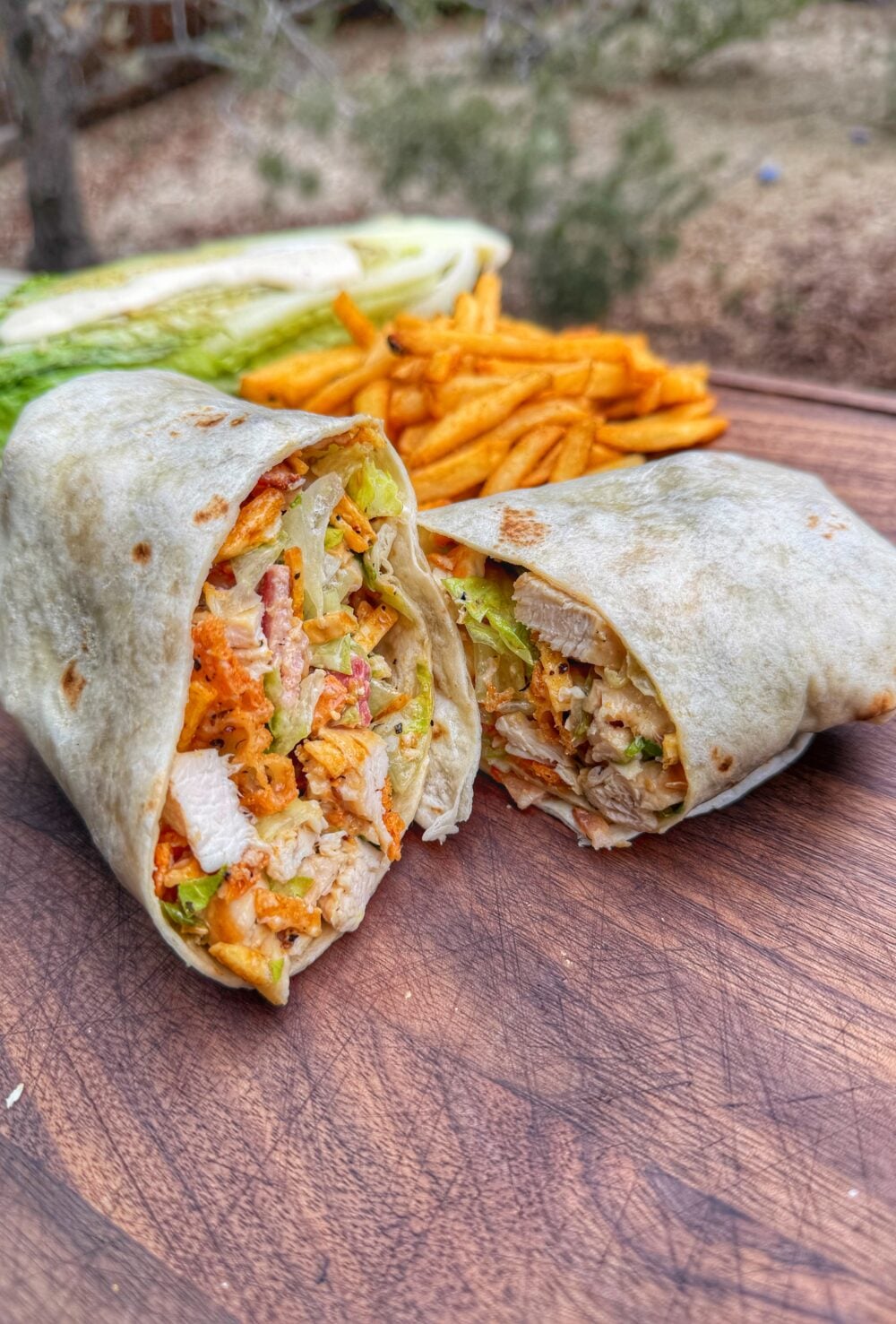 Grilled chicken Caesar wrap cut in half showing chicken, romaine, bacon, and crunchy toppings inside tortilla.