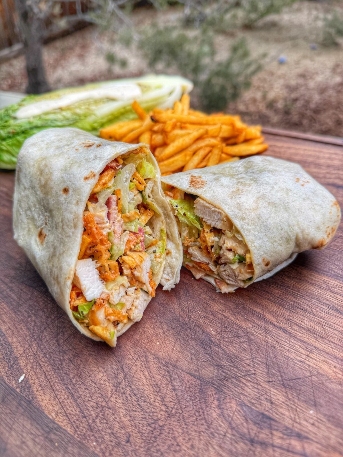 Grilled chicken Caesar wrap cut in half showing chicken, romaine, bacon, and crunchy toppings inside tortilla.