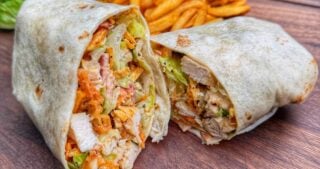 Grilled chicken Caesar wrap cut in half showing chicken, romaine, bacon, and crunchy toppings inside tortilla.