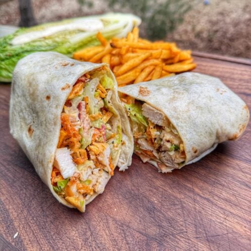 Grilled chicken Caesar wrap cut in half showing chicken, romaine, bacon, and crunchy toppings inside tortilla.