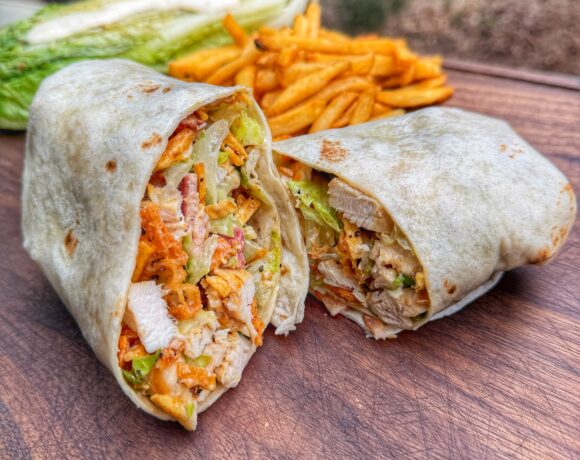 Grilled chicken Caesar wrap cut in half showing chicken, romaine, bacon, and crunchy toppings inside tortilla.