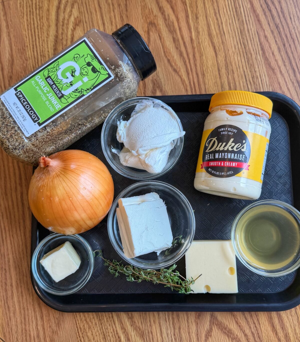 Ingredients for homemade French onion dip including onion, cream cheese, sour cream, Duke’s mayonnaise, Garlic Junkie seasoning, Swiss cheese, butter, thyme, and oil.