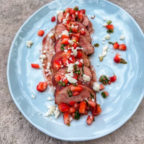 Sliced pork tenderloin topped with strawberry salsa and crumbled cotija cheese served on a light blue plate.