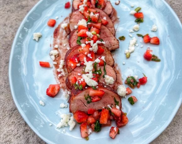 Sliced pork tenderloin topped with strawberry salsa and crumbled cotija cheese served on a light blue plate.