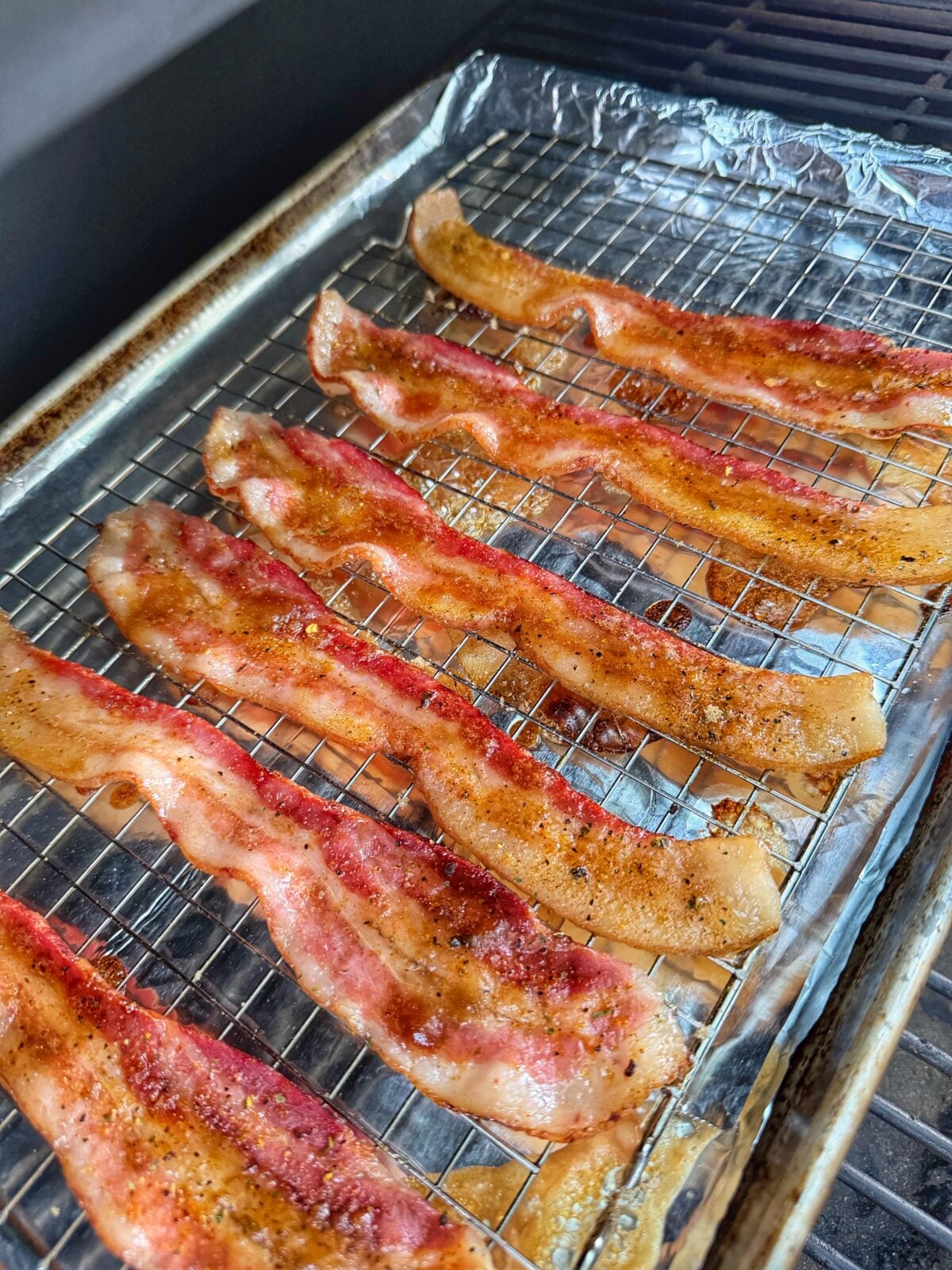 Bacon strips cooking on a wire rack inside a pellet grill with seasoning and glaze beginning to caramelize.