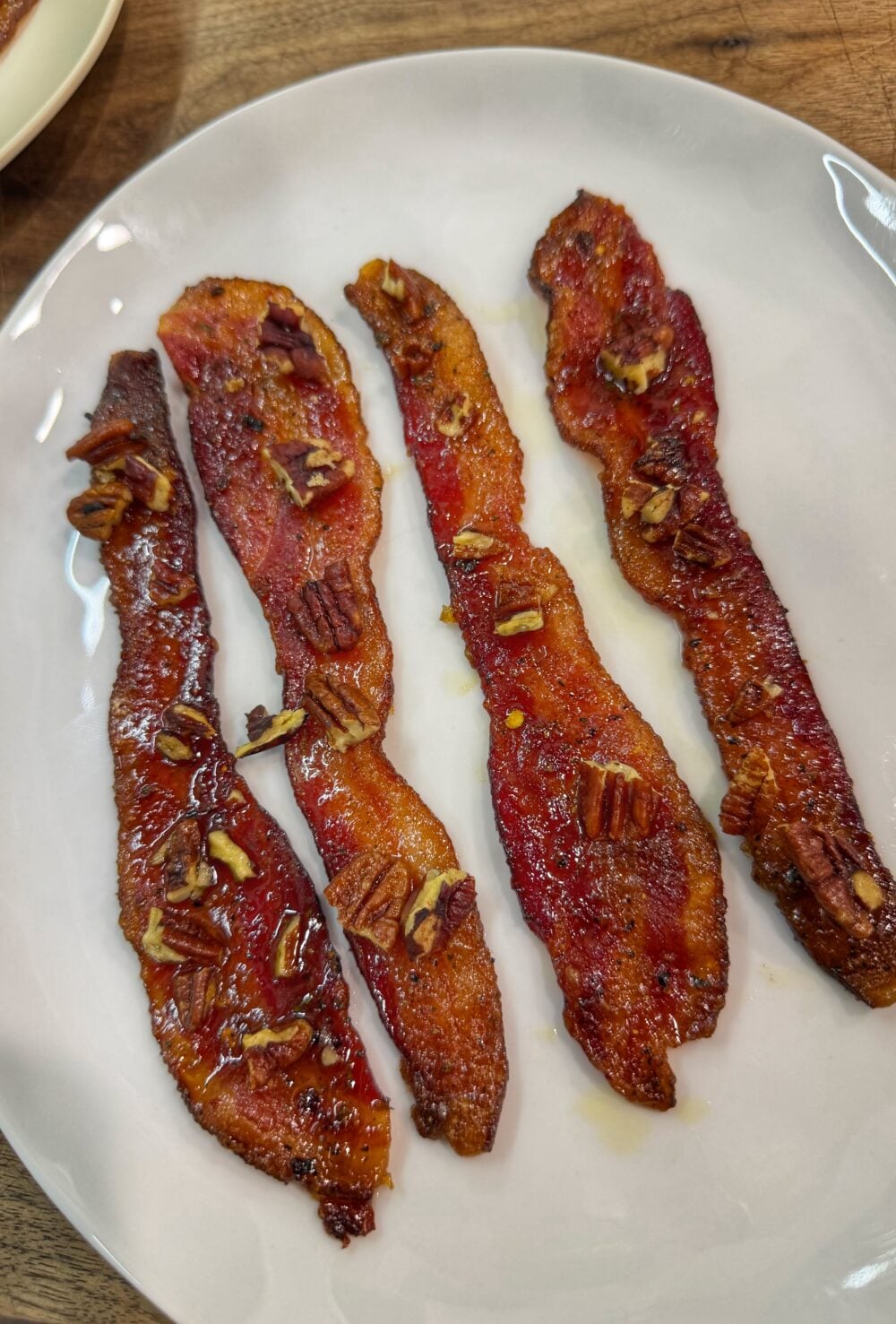Cooked candied bacon strips topped with chopped pecans on a white plate.