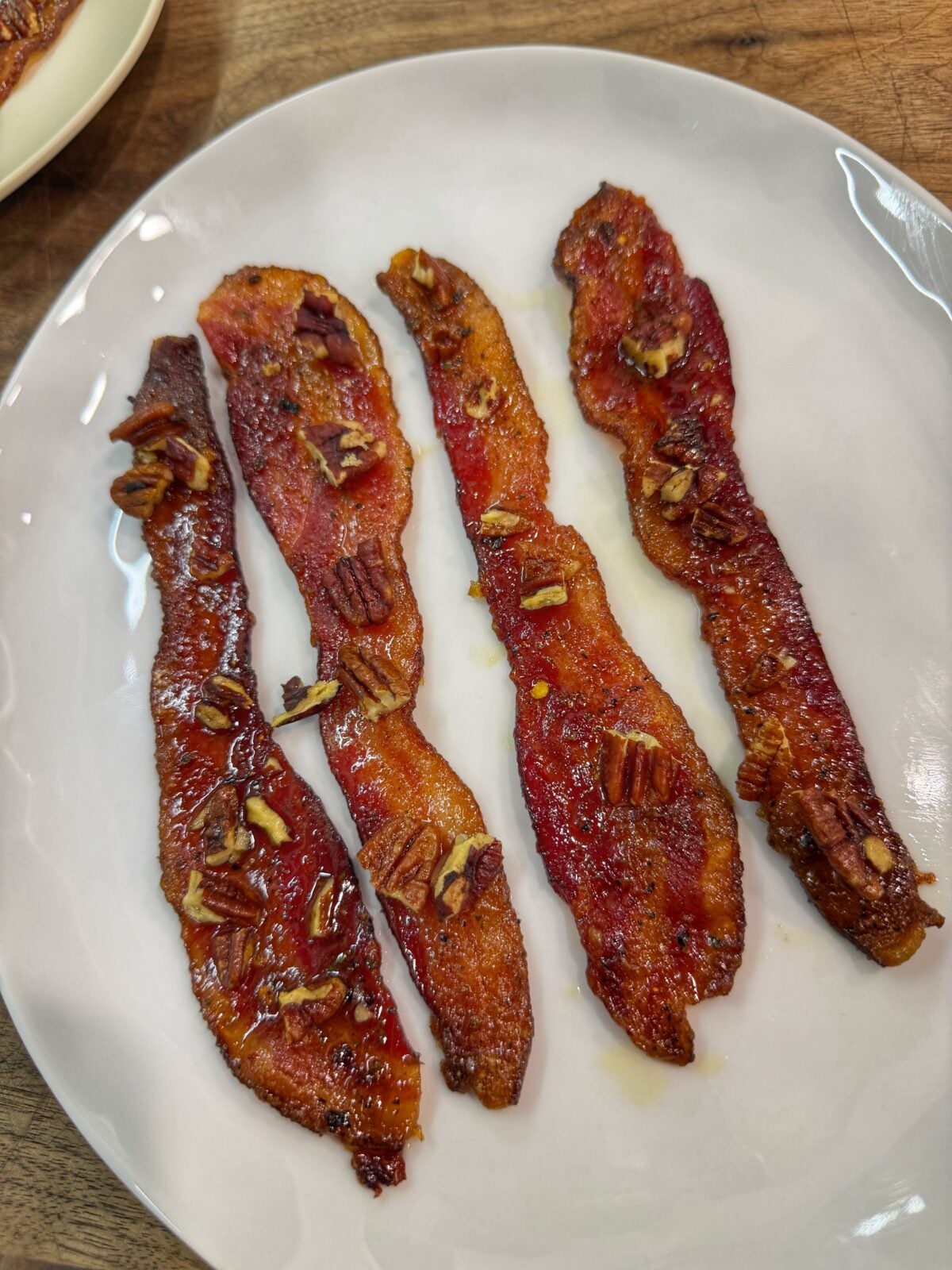 Cooked candied bacon strips topped with chopped pecans on a white plate.