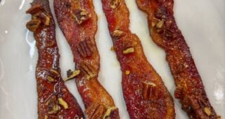 Cooked candied bacon strips topped with chopped pecans on a white plate.