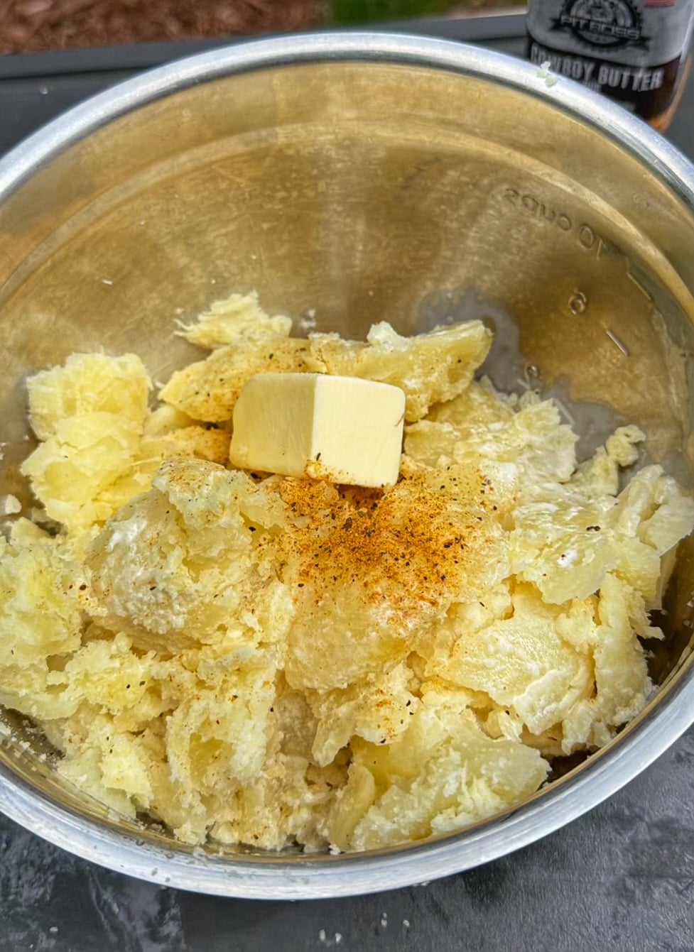 Cooked potato flesh in a mixing bowl topped with butter, sour cream, and seasoning before being mashed together.
