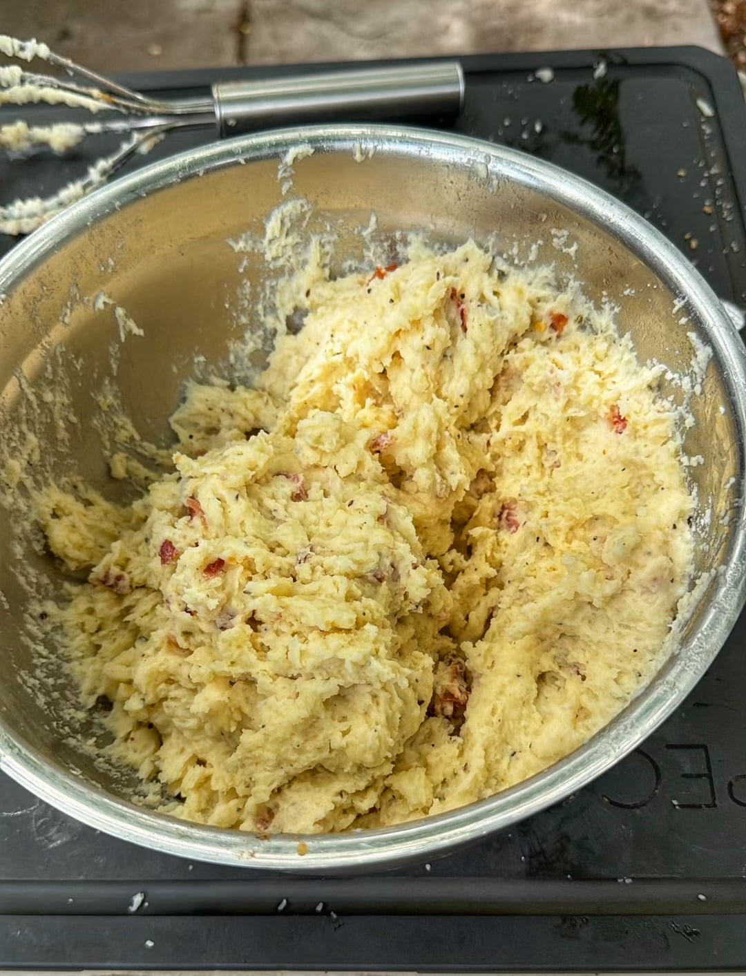 Creamy potato mixture with bacon pieces mixed together in a stainless steel bowl.