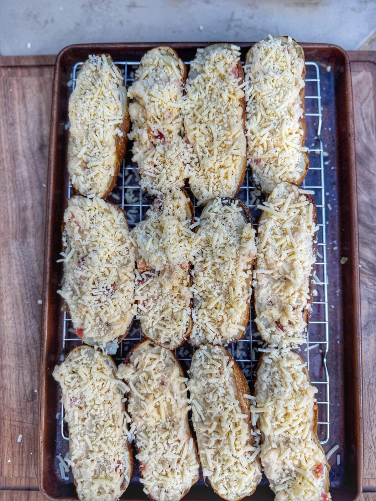 Stuffed twice baked potatoes topped with shredded cheese and arranged on a wire rack over a sheet pan.
