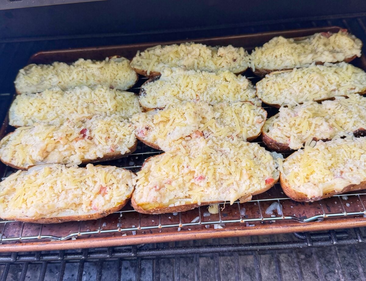 Cheese-topped twice baked potatoes cooking on a sheet pan inside a pellet grill.