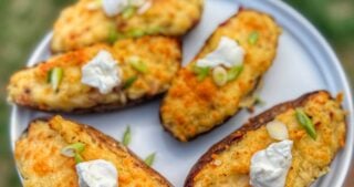 Golden brown twice baked potatoes topped with sour cream and sliced green onions on a gray plate.