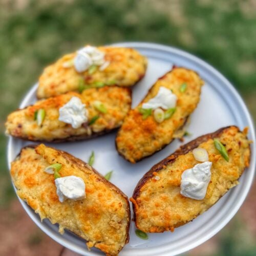 Golden brown twice baked potatoes topped with sour cream and sliced green onions on a gray plate.