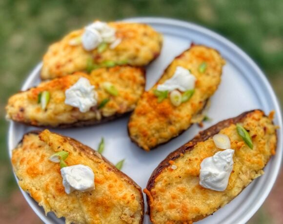 Golden brown twice baked potatoes topped with sour cream and sliced green onions on a gray plate.