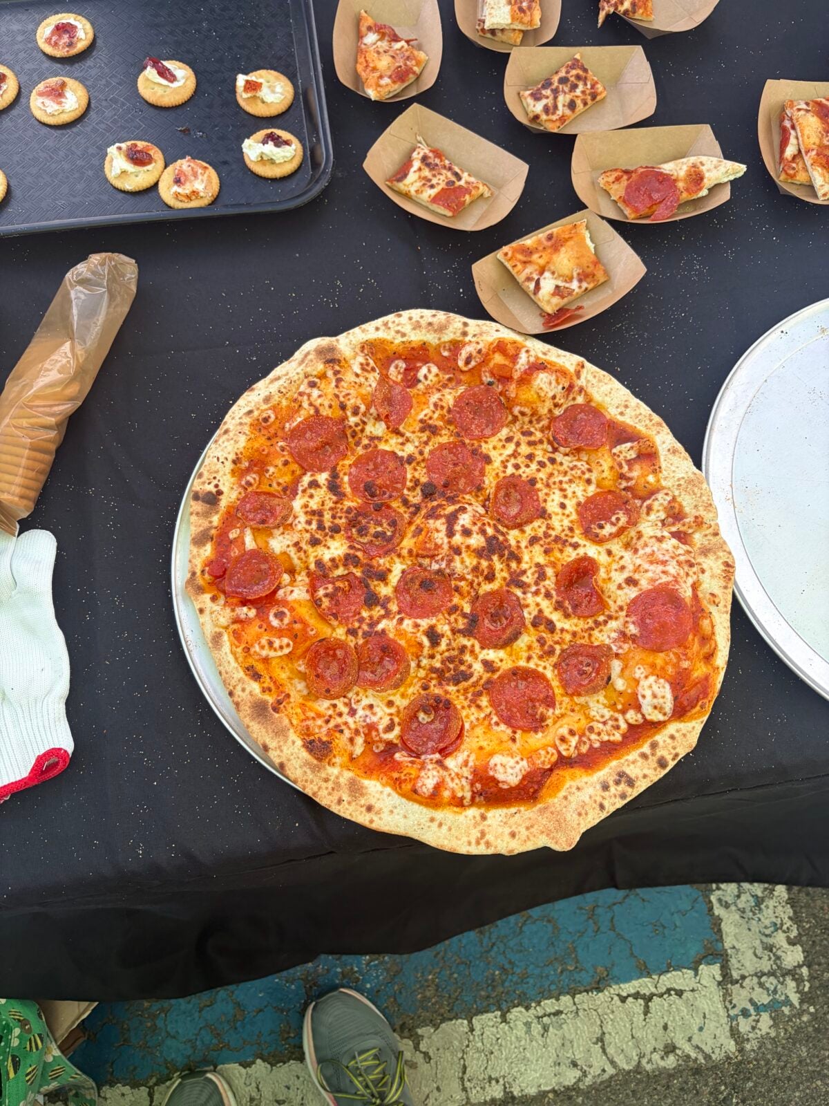 Whole pepperoni pizza on a serving tray surrounded by sample slices and smoked cream cheese crackers.