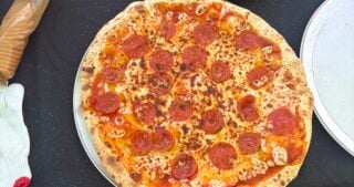 Whole pepperoni pizza on a serving tray surrounded by sample slices and smoked cream cheese crackers.