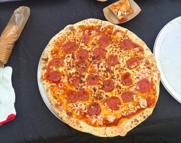 Whole pepperoni pizza on a serving tray surrounded by sample slices and smoked cream cheese crackers.