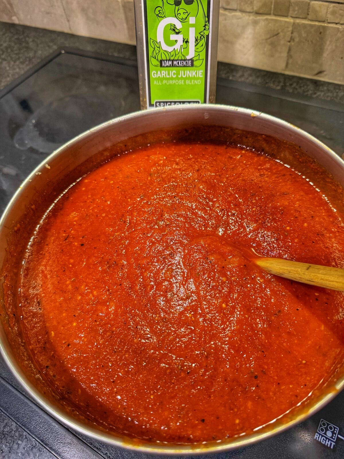 Large pot of homemade pizza sauce simmering beside a container of Garlic Junkie seasoning.