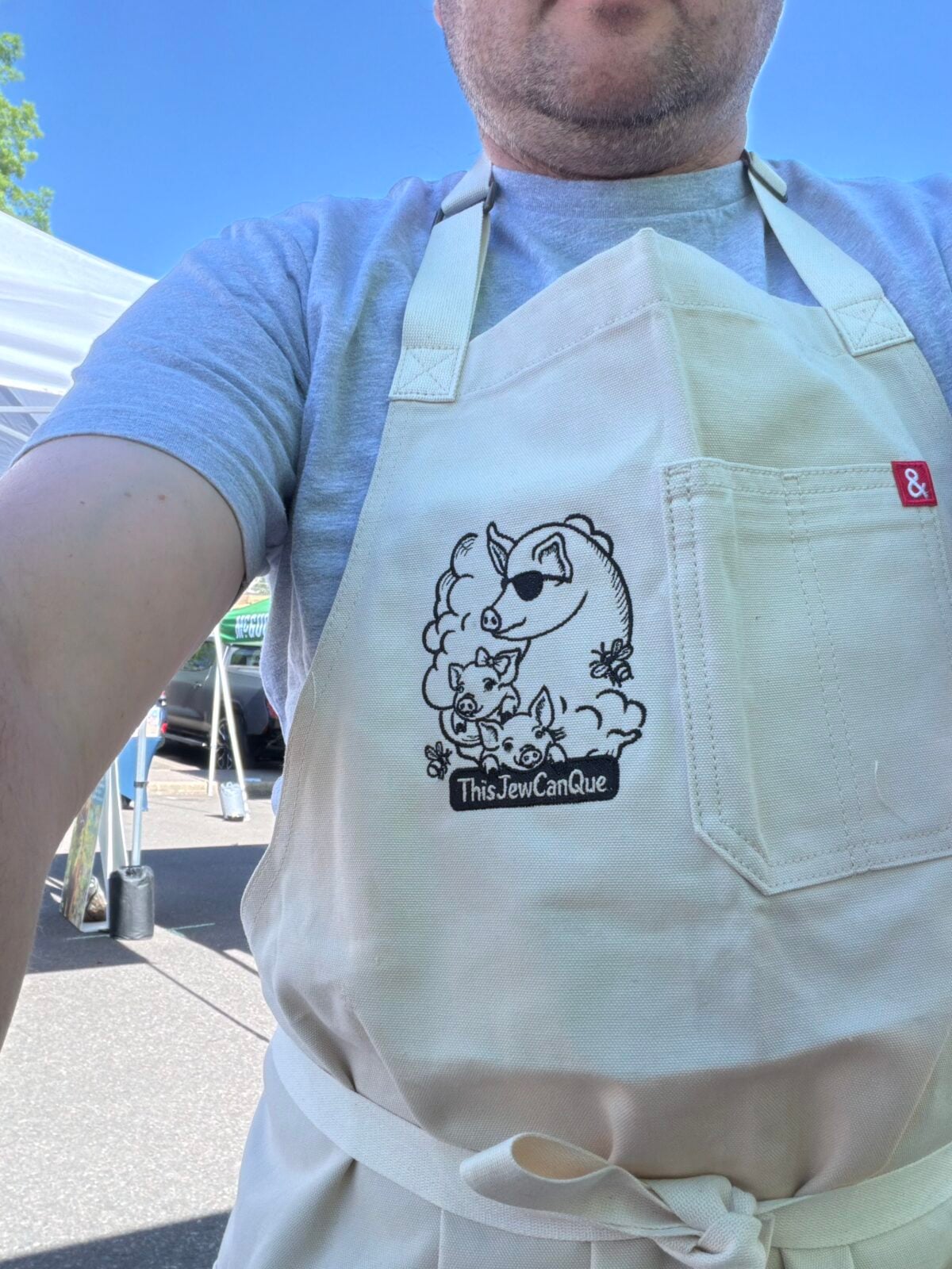 Close-up of a cream-colored apron featuring the embroidered ThisJewCanQue pig logo.