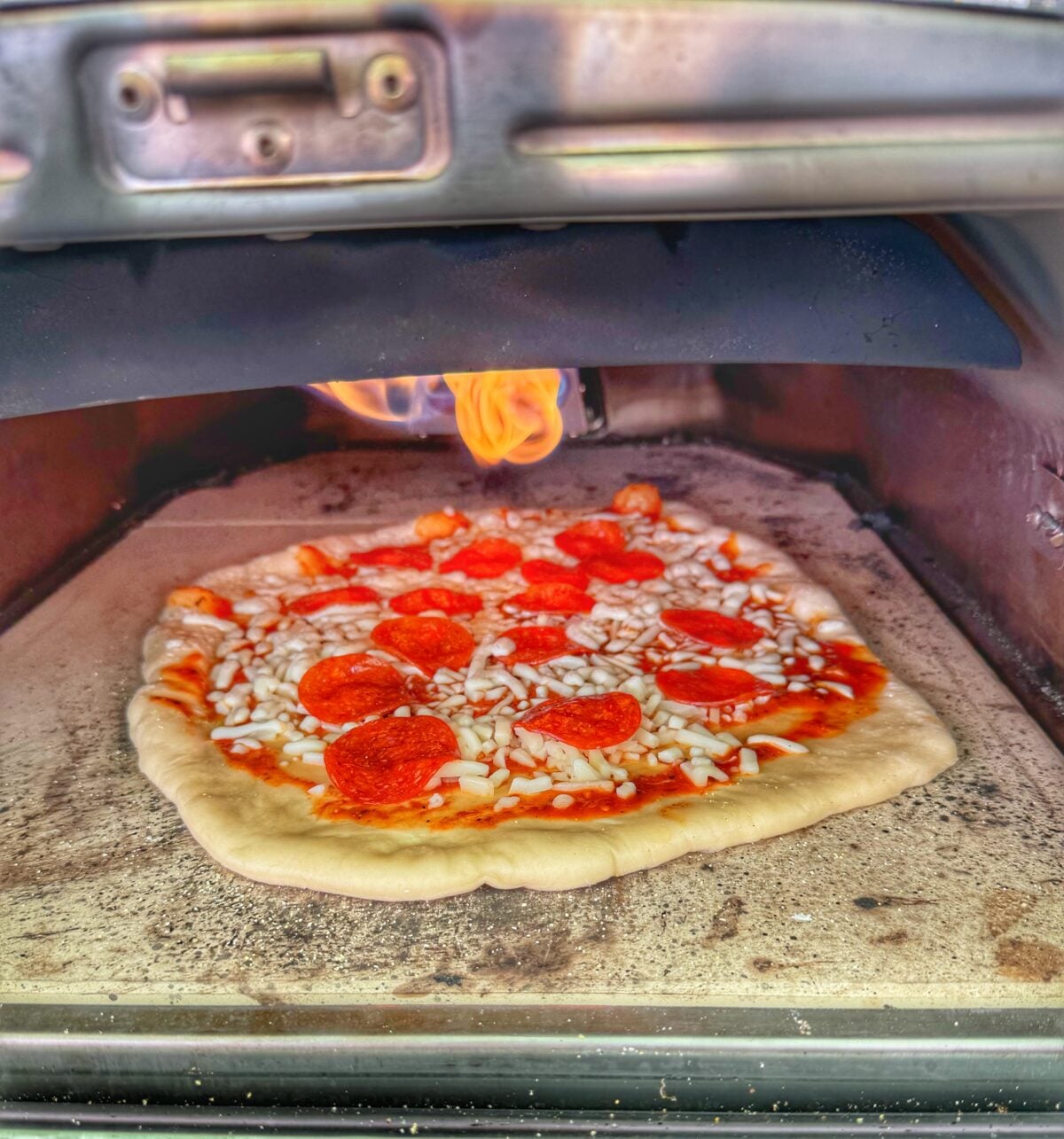 Pepperoni pizza baking inside an Ooni pizza oven with visible flame overhead.