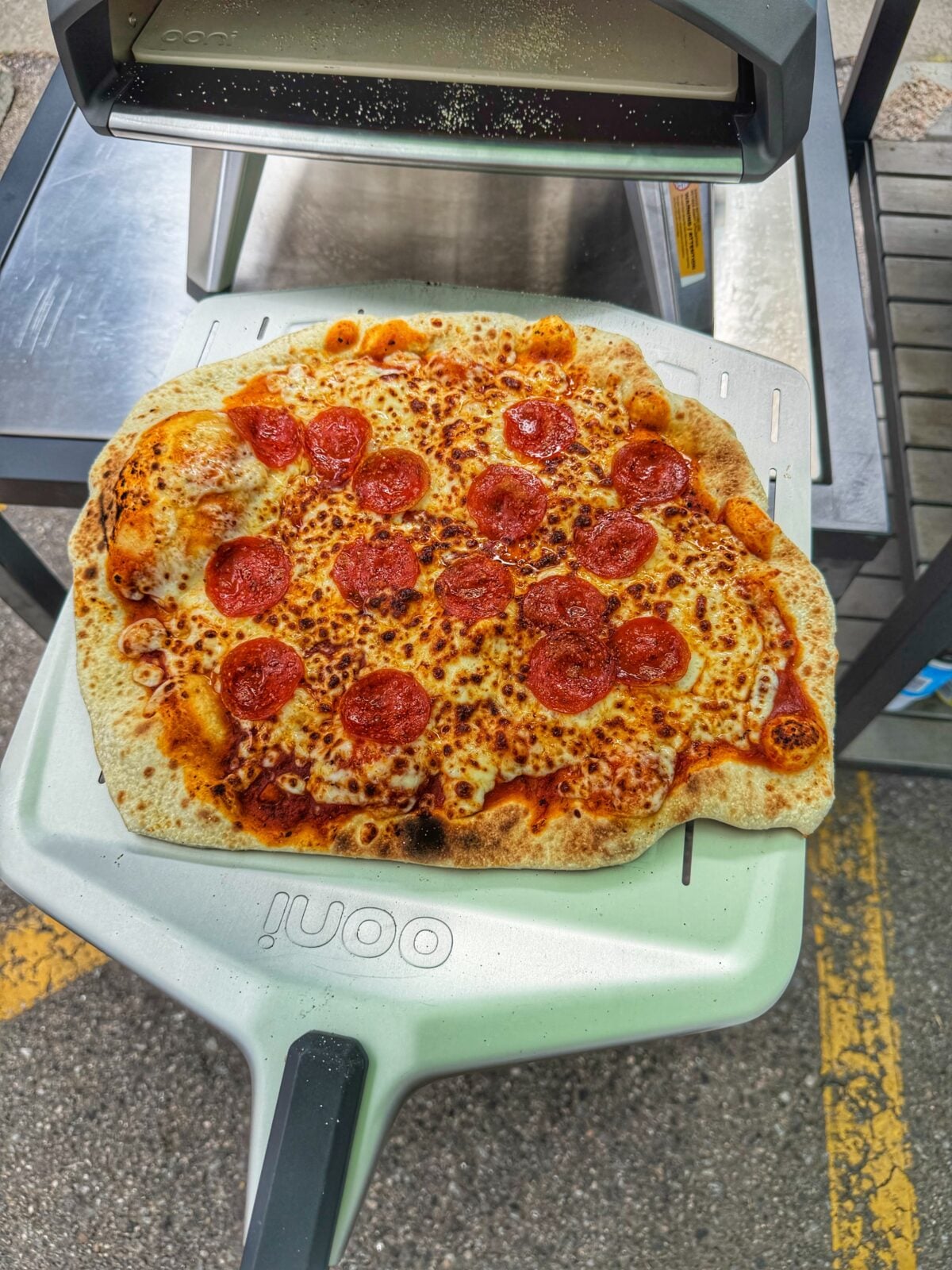 Freshly cooked pepperoni pizza resting on an Ooni pizza peel in front of the oven.