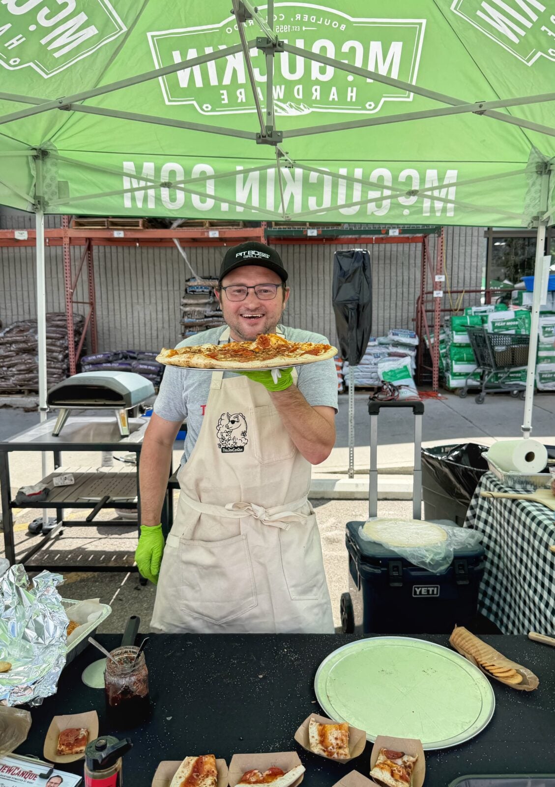 Adam McKenzie holding a freshly cooked pepperoni pizza under a McGuckin Hardware event tent.