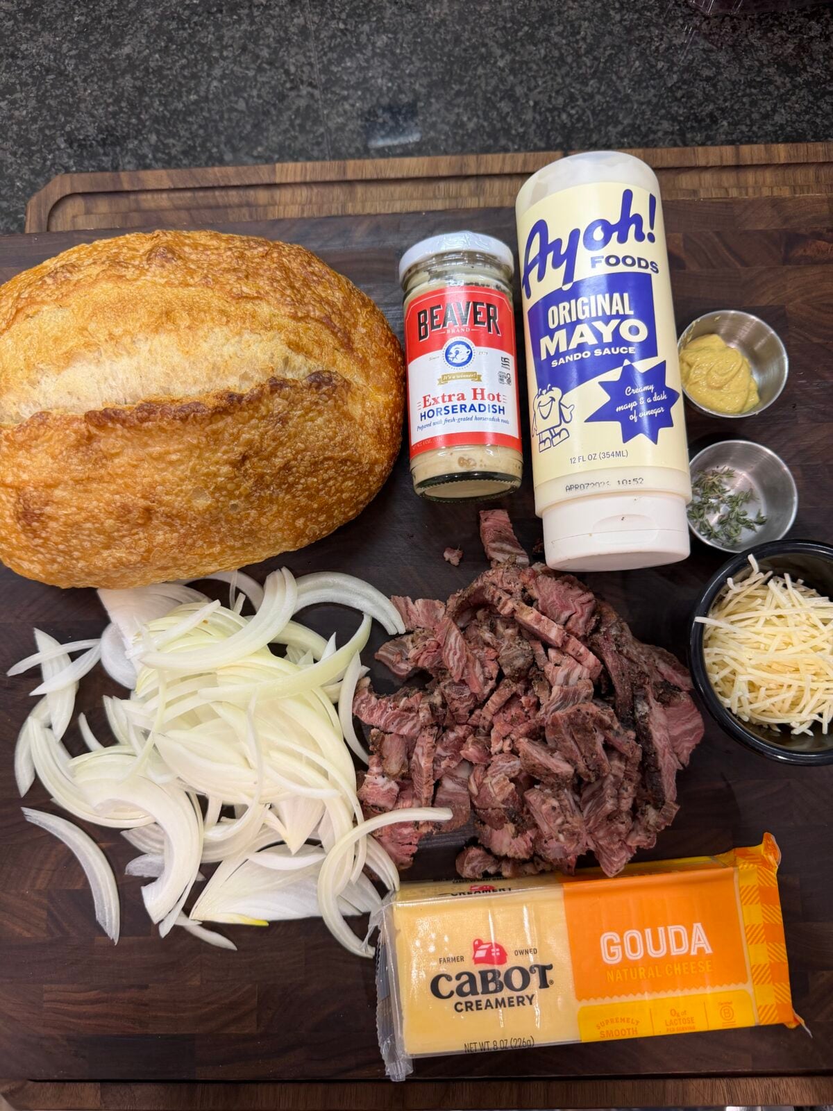 Ingredients for a French Onion Steak Melt including sourdough bread, smoked ribeye cap, Cabot Gouda cheese, sweet onions, thyme, Dijon mustard, horseradish, mayonnaise and Parmesan cheese.