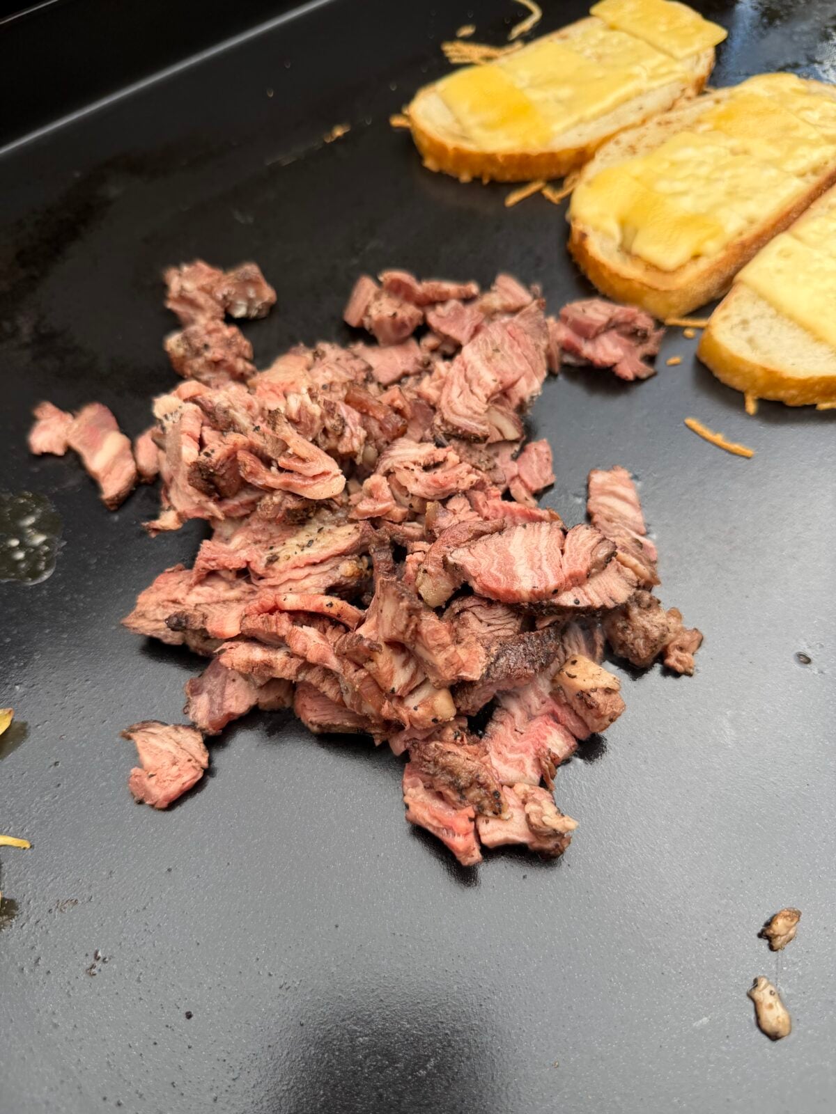 Thinly sliced leftover smoked ribeye cap warming on a Pit Boss griddle for a steak melt sandwich.