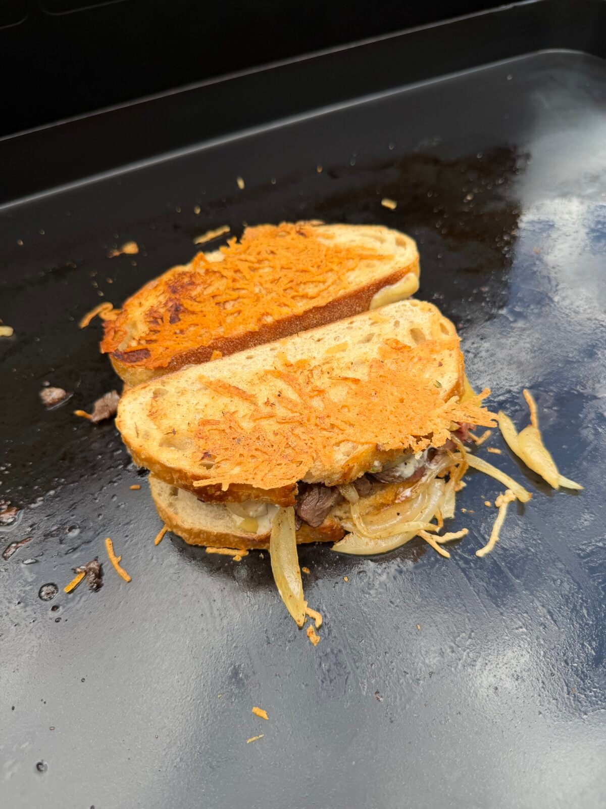 French Onion Steak Melt cooking on a Pit Boss griddle with crispy Parmesan cheese crusted onto the sourdough bread.