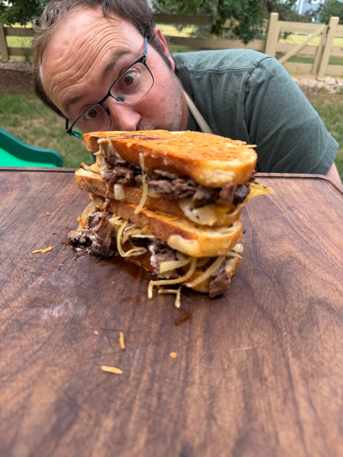 French Onion Steak Melt stacked on a cutting board with Adam from ThisJewCanQue in the background.