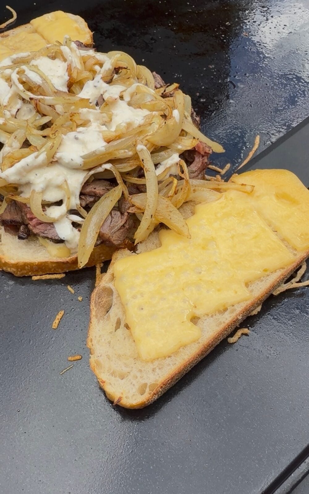French Onion Steak Melt being assembled on a Pit Boss griddle with smoked ribeye cap, caramelized thyme and Dijon onions, melted Cabot Gouda cheese, and horseradish mayo on toasted sourdough.