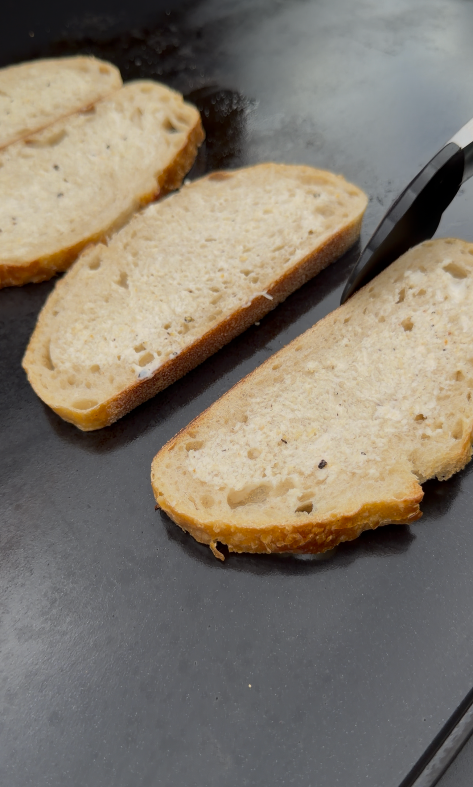 Slices of sourdough bread toasting on a Pit Boss griddle with horseradish mayo spread on the bread.