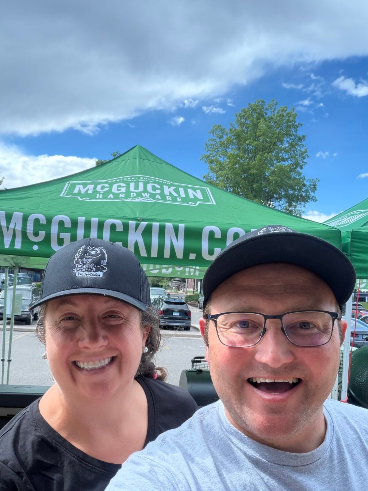 Isabel and Adam smiling beneath a green McGuckin Hardware tent during the store’s outdoor anniversary celebration.